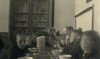 811771 Afbeelding van enkele kinderen aan een tijdens een gezamelijke maaltijd van een gaarkeuken in een lokaal in de ...